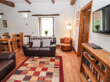 A living room with leather sofas a wooden dining table a colorful patterned rug and a wooden bookshelf at The Hayloft in Newlands near Braithwaite and Keswick