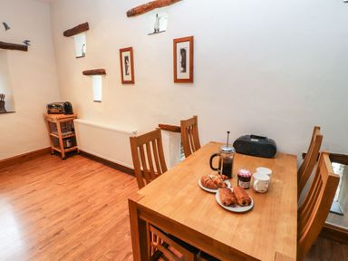 A dining area with a wooden table and chairs croissants and coffee on the table and a small wooden trolley with appliances at The Hayloft in Newlands near Braithwaite and Keswick