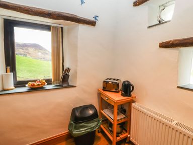 A kitchen corner with a window showing a grassy hill a wooden cart with a toaster and kettle a black trash bin and a radiator at The Hayloft in Newlands near Braithwaite and Keswick