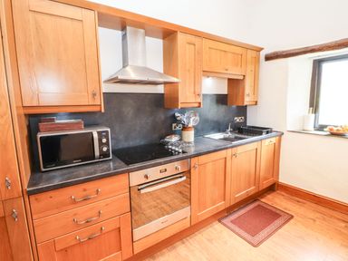 A kitchen with wooden cabinets a microwave an electric stove an oven a stainless steel sink and a window at The Hayloft in Newlands near Braithwaite and Keswick