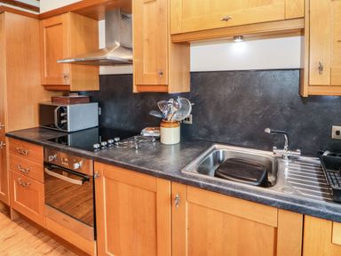 A kitchen with wooden cabinets a black countertop a stainless steel oven and sink at The Hayloft in Newlands near Braithwaite and Keswick