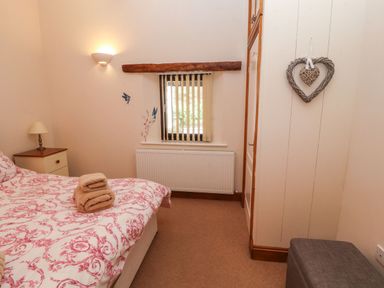 A bedroom with a bed with patterned bedding a nightstand with a lamp a window with vertical blinds and a radiator at The Hayloft in Newlands near Braithwaite and Keswick