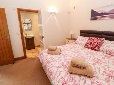 A bedroom with a bed with patterned bedding and folded towels with an open door showing a sink at The Hayloft in Newlands near Braithwaite and Keswick
