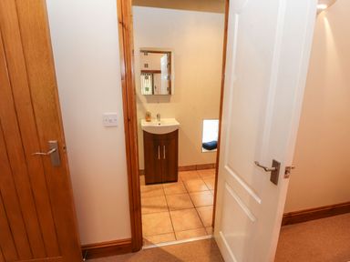A hallway with two doors and a view into a bathroom with a sink cabinet and mirror at The Hayloft in Newlands near Braithwaite and Keswick