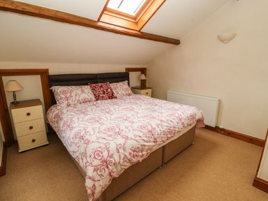 A bedroom with a double bed featuring patterned bedding two bedside tables with lamps and a skylight window at The Hayloft in Newlands near Braithwaite and Keswick