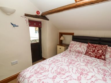 A bedroom with a bed a bedside table lamp and a door with a red blind at The Hayloft in Newlands near Braithwaite and Keswick