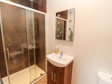 A bathroom with a glass shower enclosure a sink with a wooden cabinet a mirror and a toilet at The Hayloft in Newlands near Braithwaite and Keswick