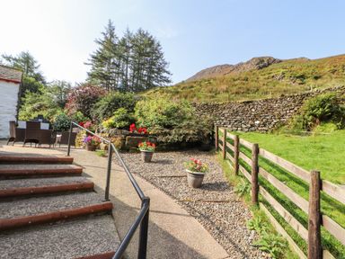 An outdoor patio area with a table and chairs next to steps and garden with plants at The Hayloft in Newlands near Braithwaite and Keswick