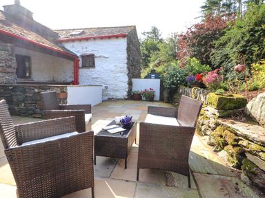 An outdoor patio with wicker chairs and a table with teapot and cup by a stone wall and garden at The Hayloft in Newlands near Braithwaite and Keswick