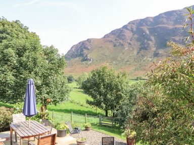 An outdoor patio with a wooden table and chairs surrounded by potted plants and trees with a mountain in the background at The Hayloft in Newlands near Braithwaite and Keswick
