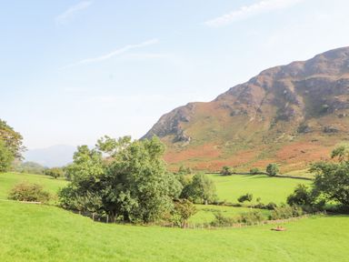 A grassy field with trees and hills in the background at The Hayloft in Newlands near Braithwaite and Keswick