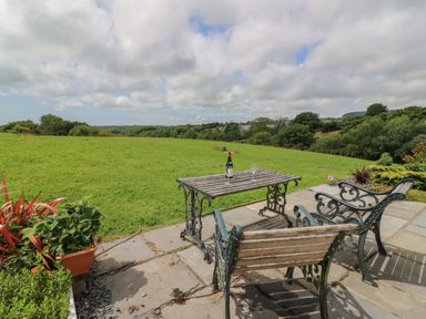 A patio with a table and two chairs overlooking a grassy field and trees at Blaenffynnon Bach in Trelech near Crymych