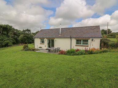 A small house with a slate roof and garden furniture on a patio surrounded by grass and flower beds at Blaenffynnon Bach in Trelech near Crymych