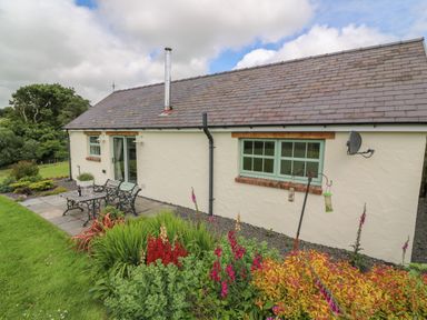 An outdoor patio with metal table and benches next to a cream cottage with green windows and colorful garden at Blaenffynnon Bach in Trelech near Crymych