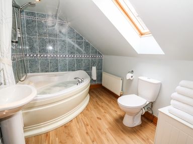 A bathroom with a bathtub a toilet a sink and stacked towels near a skylight window at Tangaer Cottage in Cellan near Lampeter