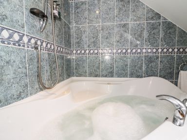 A bathroom with a filled bathtub and tiled walls at Tangaer Cottage in Cellan near Lampeter