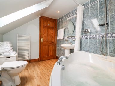 A bathroom with a bathtub full of water a toilet a sink a wooden door and folded towels on a storage unit at Tangaer Cottage in Cellan near Lampeter