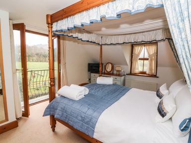 A bedroom with a four poster bed a blue quilt and white towels by a window and glass door at Tangaer Cottage in Cellan near Lampeter