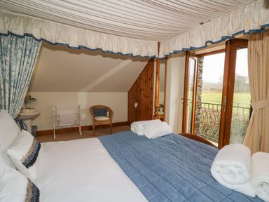 A bedroom with a double bed near a balcony door and a chair at Tangaer Cottage in Cellan near Lampeter
