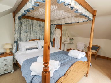 A bedroom with a wooden four-poster bed with blue and white bedding a bedside table with lamp a wicker chair and a sink area at Tangaer Cottage Cellan near Lampeter