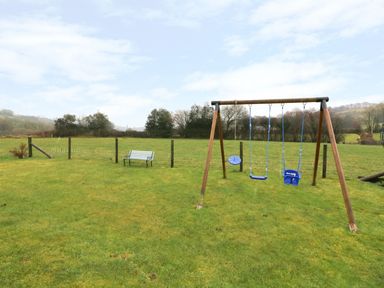 An outdoor swing set with three blue swings and a white bench in a grassy fenced field at Tangaer Cottage in Cellan near Lampeter