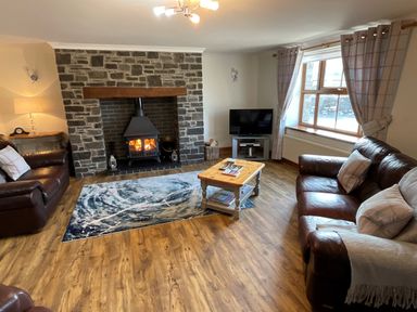 A living room with a stone fireplace wood burner two leather sofas a wooden coffee table a television and window with curtains at Tangaer Cottage in Cellan near Lampeter