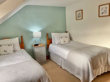 A bedroom with two single beds a nightstand with a lamp and framed pictures on the wall at Tangaer Cottage in Cellan near Lampeter