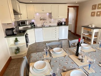A kitchen with white cabinets dining table set for four with plates bowls and wine at Tangaer Cottage in Cellan near Lampeter