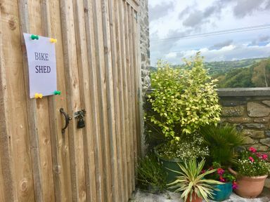 Wooden door with a bike shed sign and several potted plants outside near a stone wall at Tangaer Cottage in Cellan near Lampeter