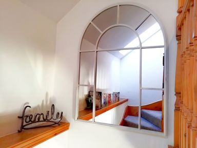 A staircase with wooden handrails visible in a mirror and a metal decoration spelling family on a wooden ledge at Tangaer Cottage in Cellan near Lampeter