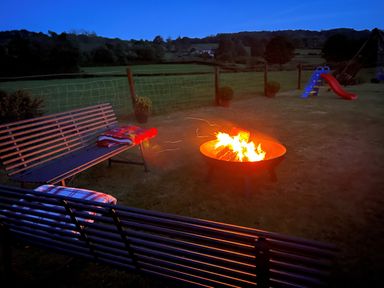 An outdoor seating area with benches and a fire pit in a grassy yard with a slide and swing set at Tangaer Cottage in Cellan near Lampeter