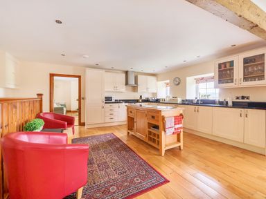 A kitchen with white cabinets a wooden island two red chairs and a patterned rug at Old Rectory Cottages Aberhafesp near Newtown