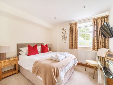 A bedroom with a bed featuring red pillows bedside tables lamps a chair curtains and a wall-mounted television at Old Rectory Cottages Aberhafesp near Newtown