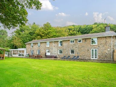 A stone house with picnic tables a hot tub and lounge chairs on a lawn at Old Rectory Cottages Aberhafesp near Newtown