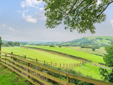 A green field with wooden fences and hills in the background at Old Rectory Cottages Aberhafesp near Newtown