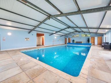 An indoor swimming pool with blue water surrounded by tiled floor and seating areas at Old Rectory Cottages Aberhafesp near Newtown