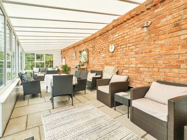 A conservatory with wicker chairs and a dining table against a brick wall at Old Rectory Cottages Aberhafesp near Newtown