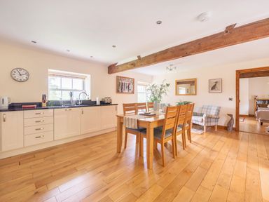 A kitchen and dining area with a wooden dining table and six chairs a sink a window a clock and a small couch at Old Rectory Cottages Aberhafesp near Newtown
