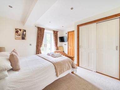 A bedroom with a bed blankets pillows a TV curtains and a closet at Old Rectory Cottages Aberhafesp near Newtown