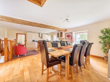 A dining area with a wooden table and eight black chairs next to a kitchen with white cabinets and two red armchairs at Old Rectory Cottages Aberhafesp near Newtown