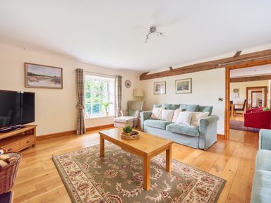 A living room with a wooden coffee table a blue sofa with cushions an armchair and a television at Old Rectory Cottages Aberhafesp near Newtown