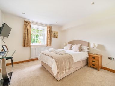A bedroom with a double bed side tables a window with curtains and a wall mounted TV at Old Rectory Cottages Aberhafesp near Newtown