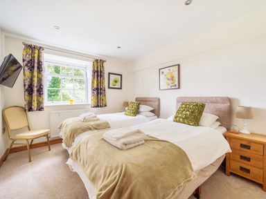 A bedroom with two single beds a chair a wall mounted tv and a window with curtains at Old Rectory Cottages Aberhafesp near Newtown