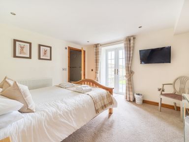 A bedroom with a wooden bed towels on bed framed pictures on the wall a wall mounted tv and a chair at Old Rectory Cottages Aberhafesp near Newtown