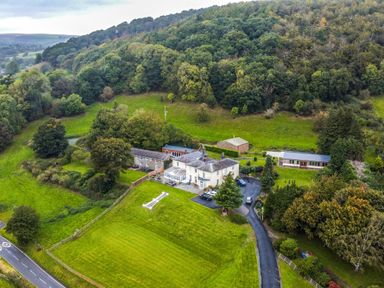 An aerial view of a house with multiple buildings a driveway and trees on a hillside at Old Rectory Cottages Aberhafesp near Newtown