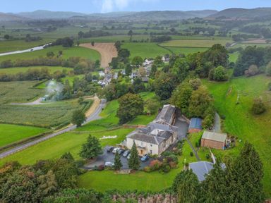 An aerial view of a countryside estate with buildings, paved parking area with cars, surrounding greenery and farmland at Old Rectory Cottages Aberhafesp near Newtown