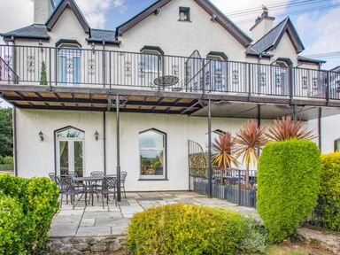 An exterior view of a two-story house with a balcony and patio furniture on a paved area at Menai View in Llanfairpwllgwyngyll near Beaumaris