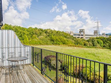 A balcony with a metal table and two chairs overlooking a grassy field and trees at Menai View in Llanfairpwllgwyngyll near Beaumaris