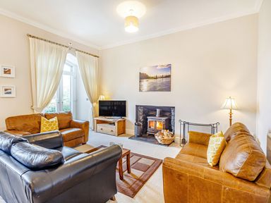 A living room with leather sofas a television and a wood burning stove at Menai View in Llanfairpwllgwyngyll near Beaumaris