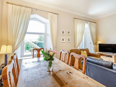 A dining area with a wooden table and chairs next to a living room with sofas and a television at Menai View in Llanfairpwllgwyngyll near Beaumaris